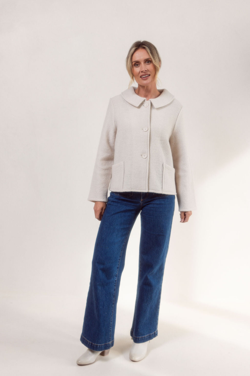 Woman wearing a cream See Saw boiled wool jacket and blue jeans on a white background
