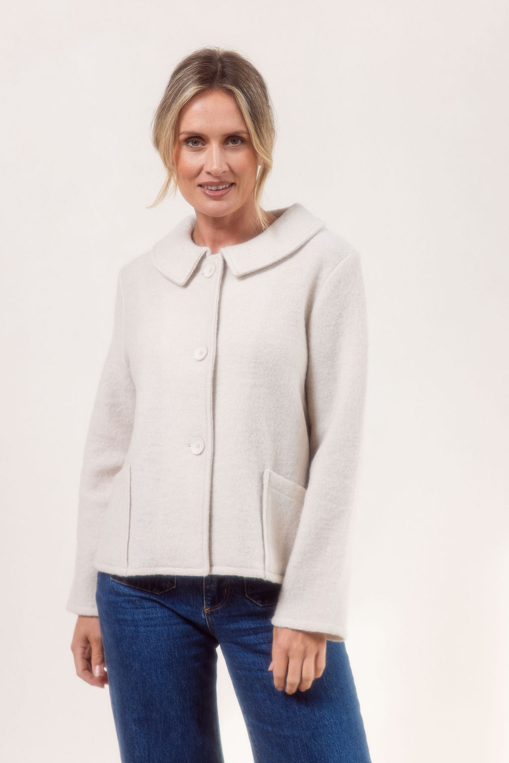 Woman wearing a cream See Saw boiled wool jacket and blue jeans on a white background