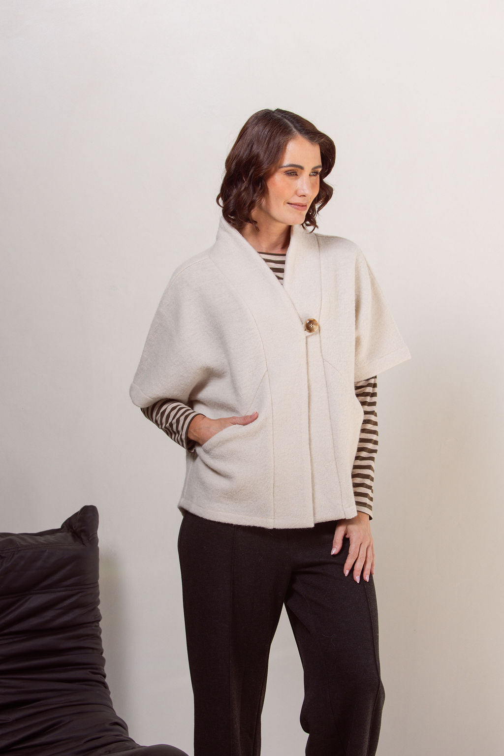Woman wearing a See Saw boiled wool cream-colored cape jacket with striped sleeves against a plain background