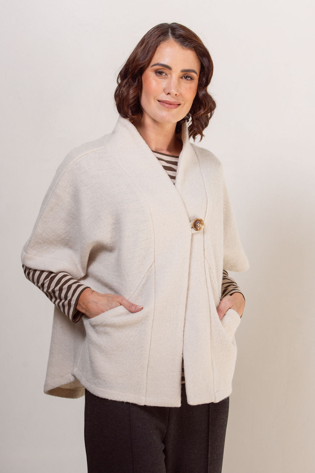 Woman wearing a See Saw boiled wool cream-colored cape jacket with striped sleeves against a plain background