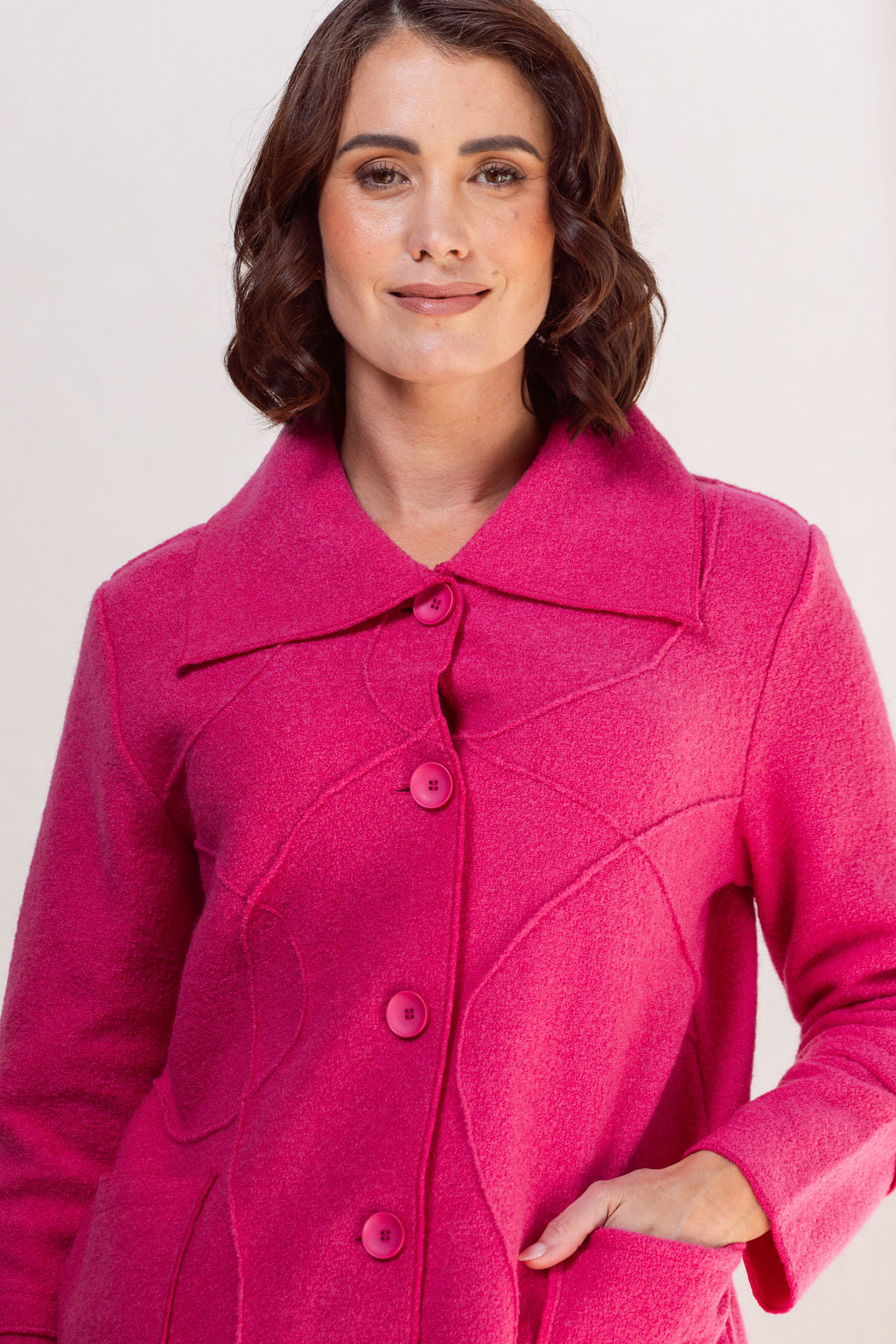 Woman wearing a bright pink See Saw Boiled wool coat against a plain background