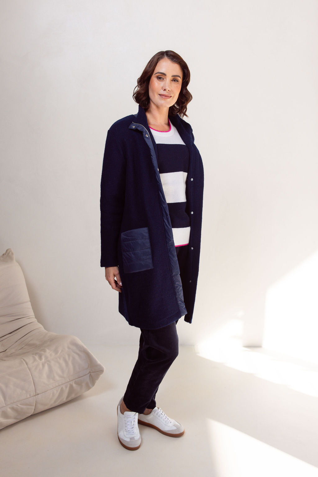Woman wearing a navy boiled wool See Saw coat over a patterned sweater on a plain background