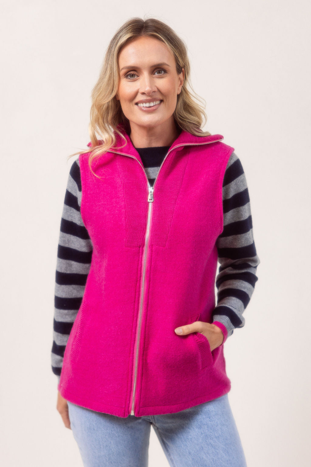 Woman wearing a See Saw pink zip-up vest over a white shirt with a plain background.