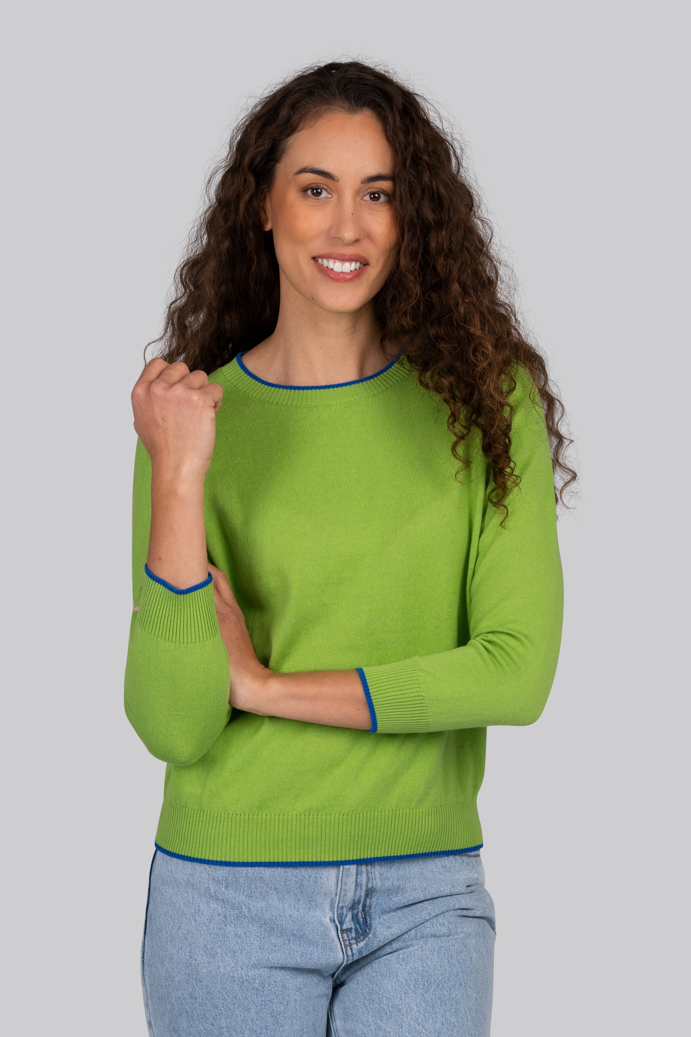Woman wearing a green Kaleido cotton cashmere sweater with blue trim on a gray background
