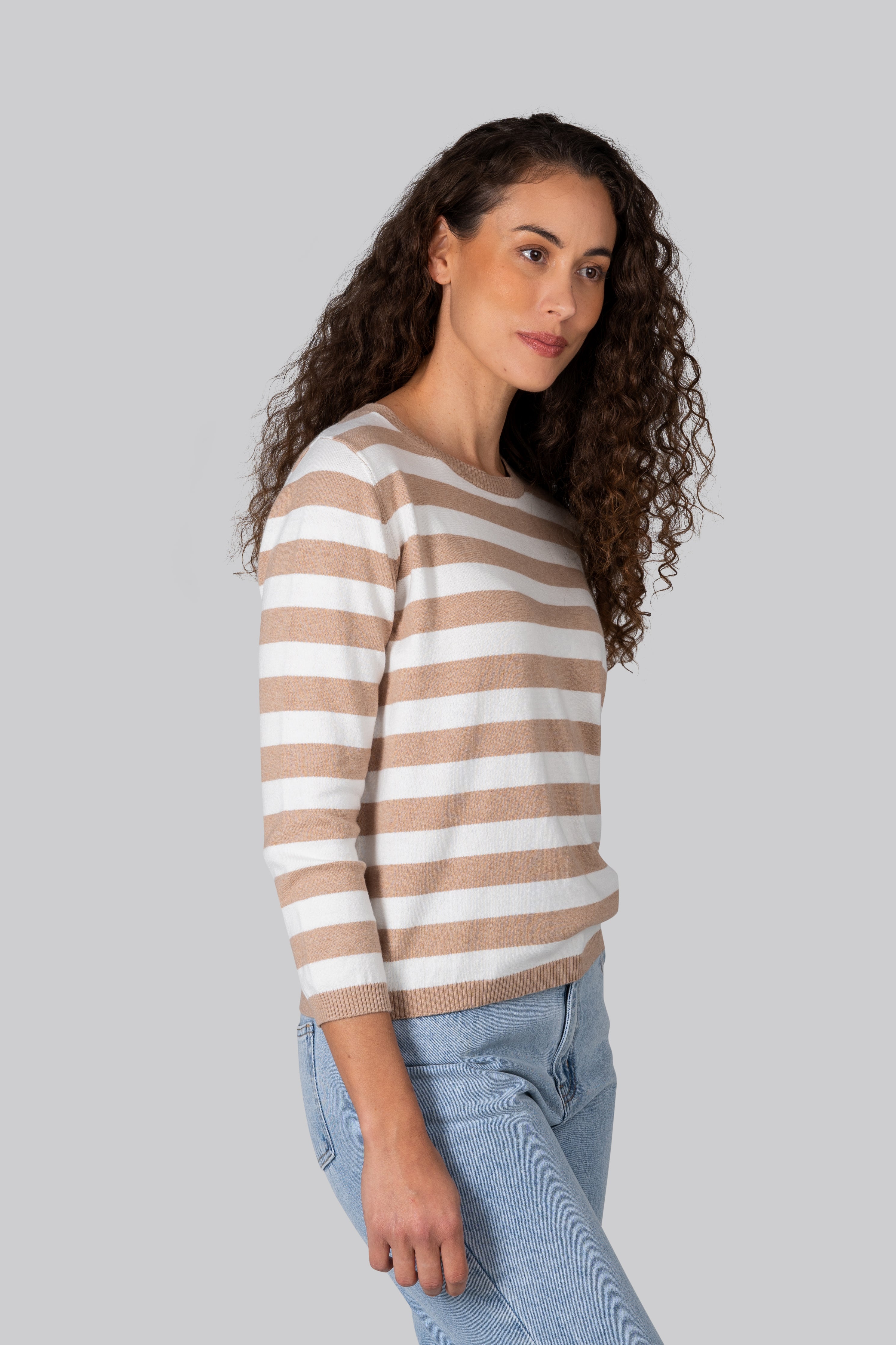 Woman wearing a cotton cashmere Kaleido striped sweater and jeans against a plain background