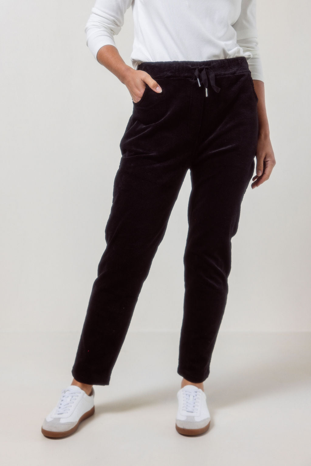 Person wearing See Saw Navy corduroy jogger pants and white sneakers on a plain background