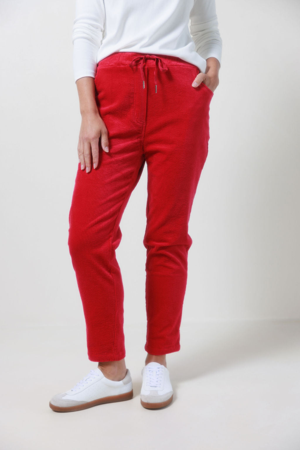 Person wearing See Saw red corduroy jogger pants and white sneakers on a plain background