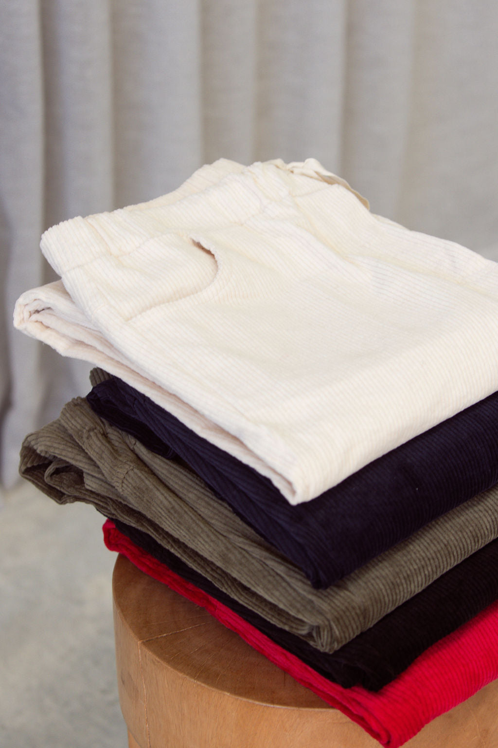 Stack of folded See Saw Cord Joggers on a wooden stool with a neutral background