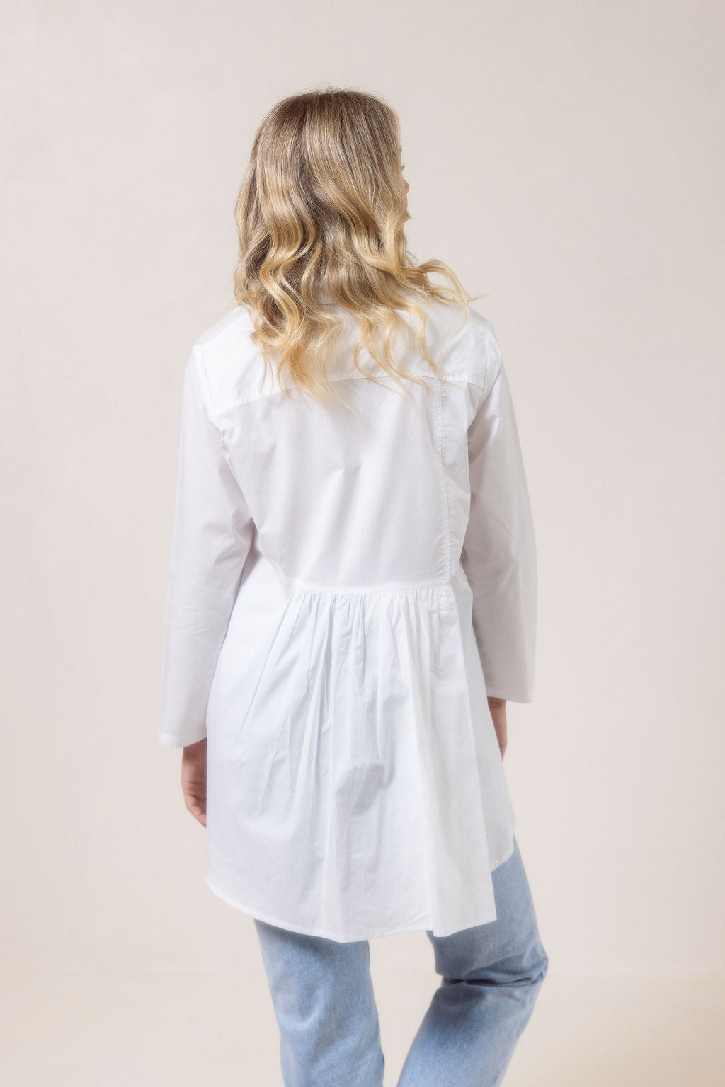 Woman wearing a white See Saw shirt in cotton with a gathered back and blue jeans against a plain background