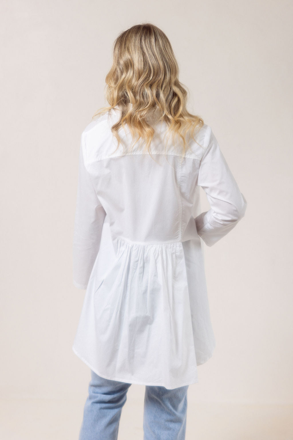Woman wearing a white See Saw shirt in cotton with a gathered back and blue jeans against a plain background