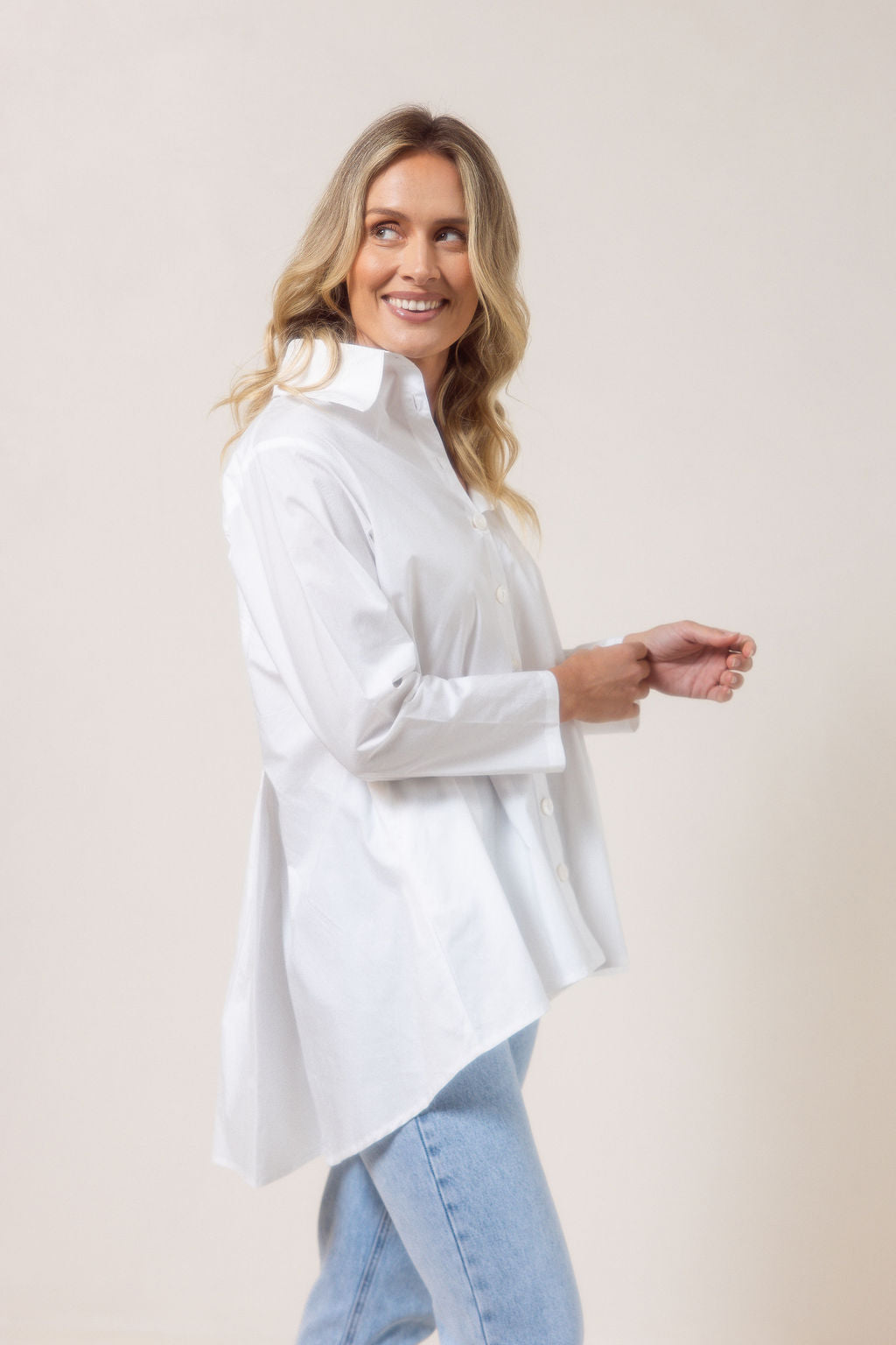 Woman wearing a white See Saw shirt in cotton with a gathered back and blue jeans against a plain background
