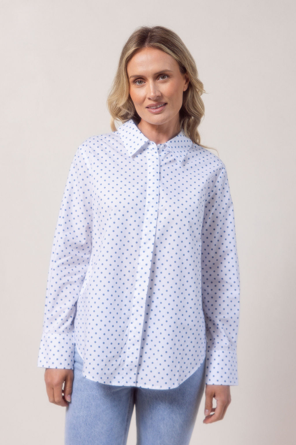 Woman wearing a classic white See Saw shirt with spot detail in a bright room with a vase and plant in the background
