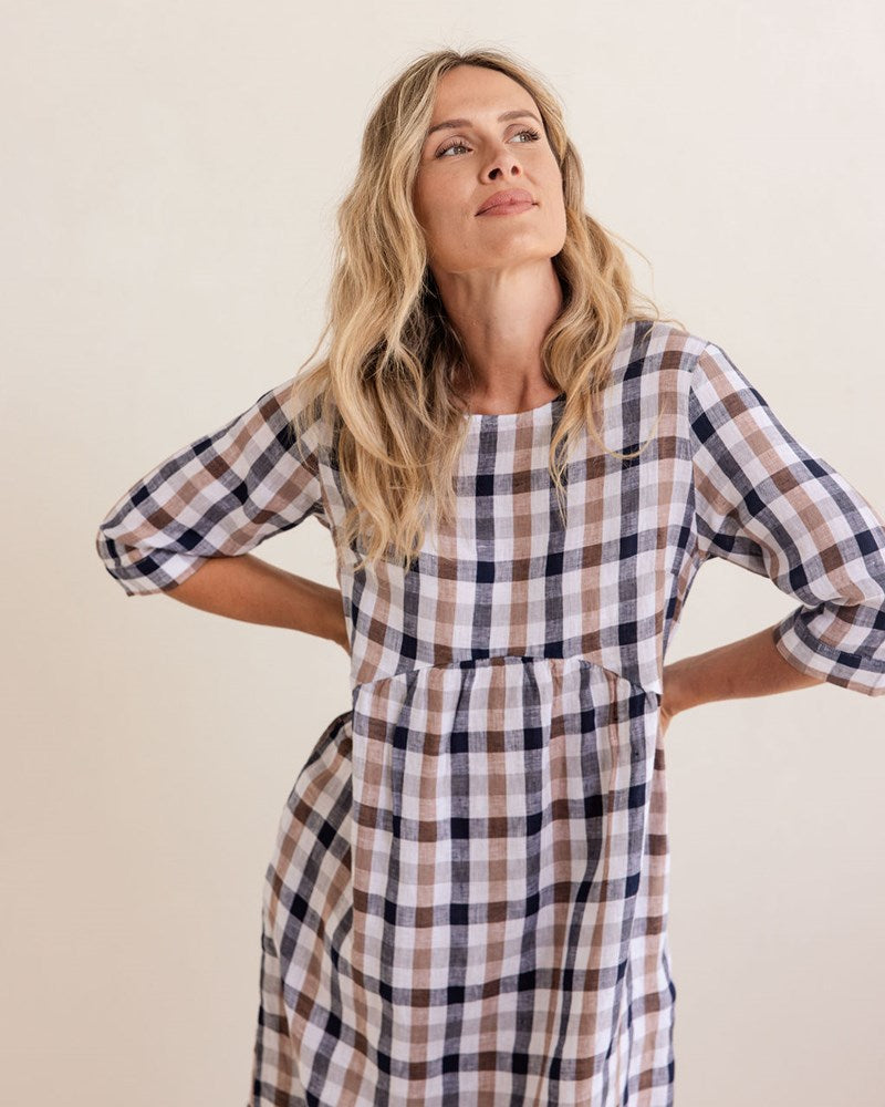 Woman wearing a blue and white checkered dress standing next to a decorative vase against a plain background. See Saw Linen Elbow Sleeve Button Back Dress