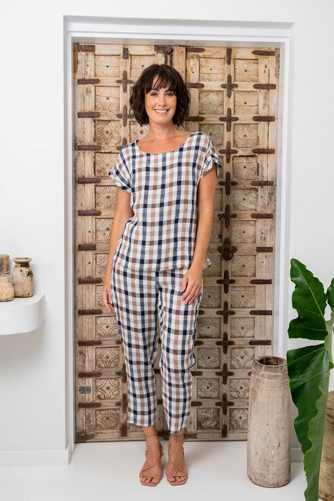 Woman in a checkered outfit standing in front of a decorative wooden door. See Saw Linen Check Cap Sleeve Top