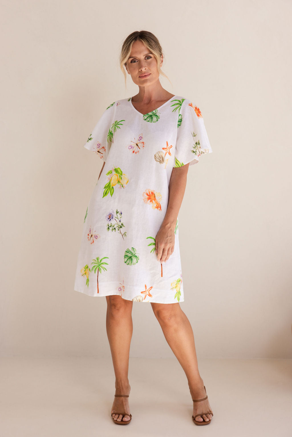 Woman wearing a white dress with colorful floral pattern on a beige background. See Saw Linen V Neck Flutter Sleeve Midi Dress