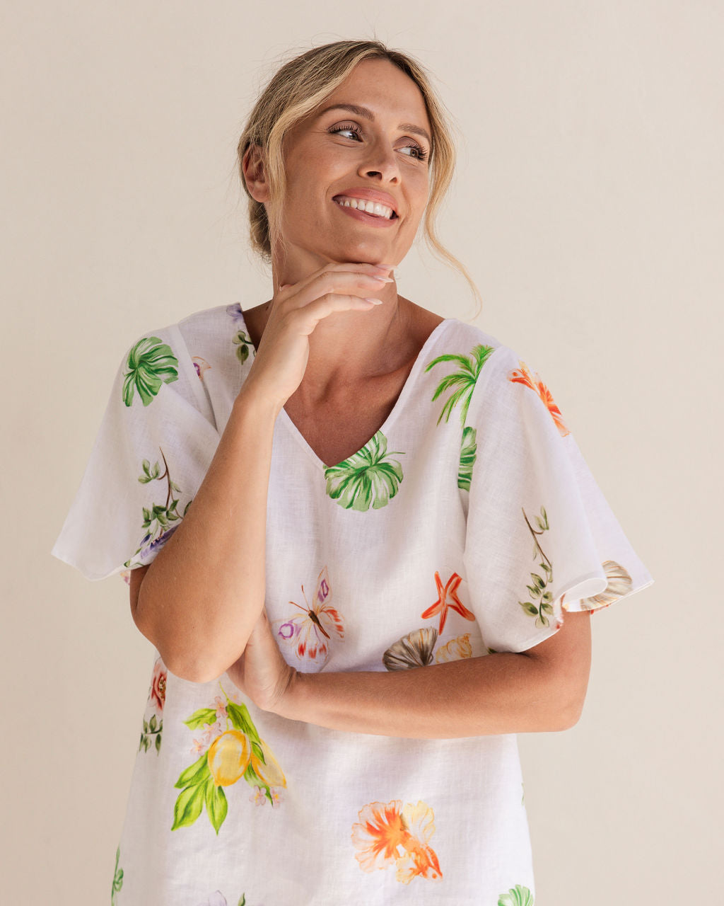 Woman wearing a white dress with colorful floral patterns against a plain background. See Saw Linen V Neck Flutter Sleeve Midi Dress
