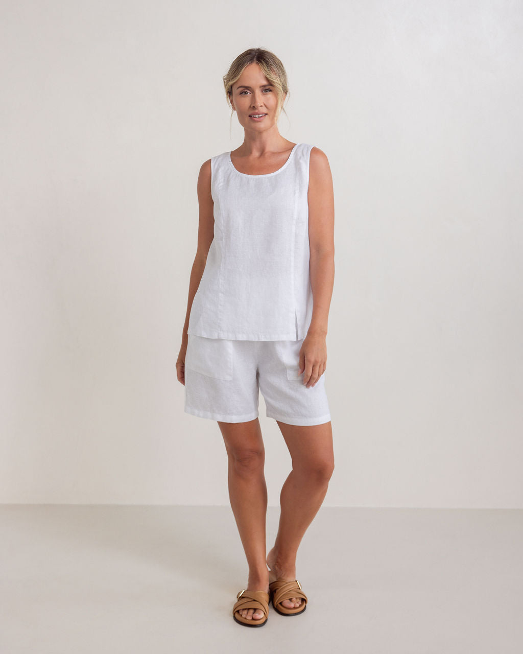 Woman wearing a white linen See Saw sleeveless top and shorts against a white background