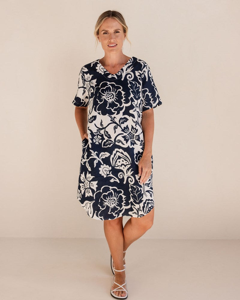 Woman wearing a navy floral dress on a beige background. See Saw Linen Soft V Neck Print Dress