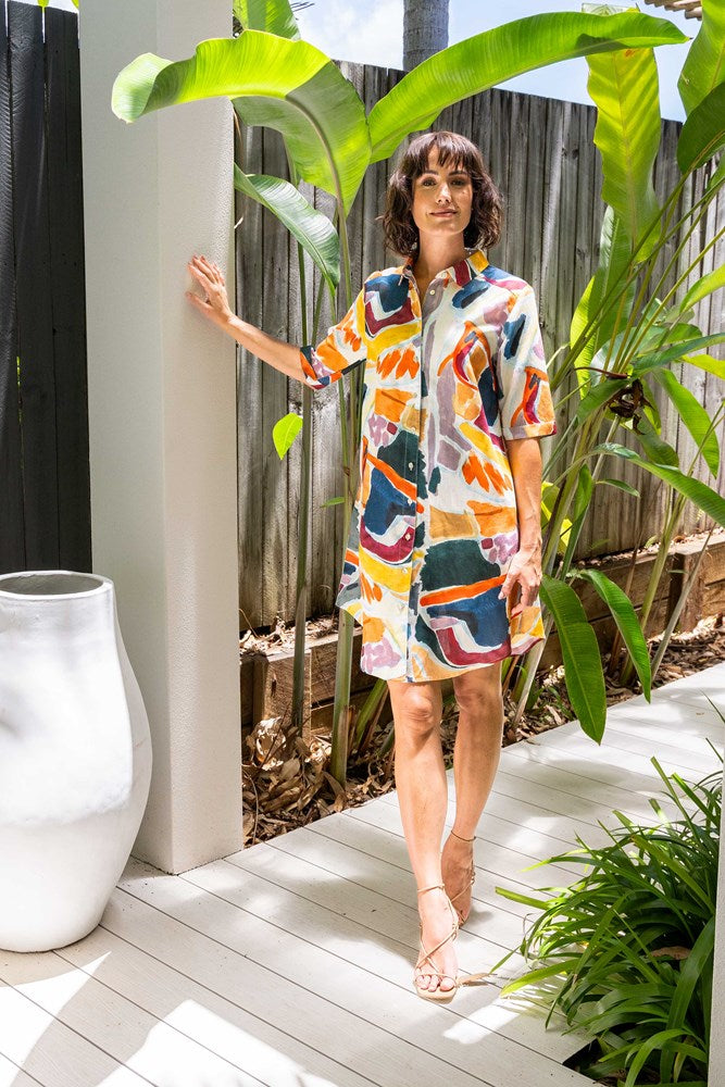Woman in a colorful dress standing outdoors with plants and a white vase in the background. See Saw Linen Shirtmaker Dress