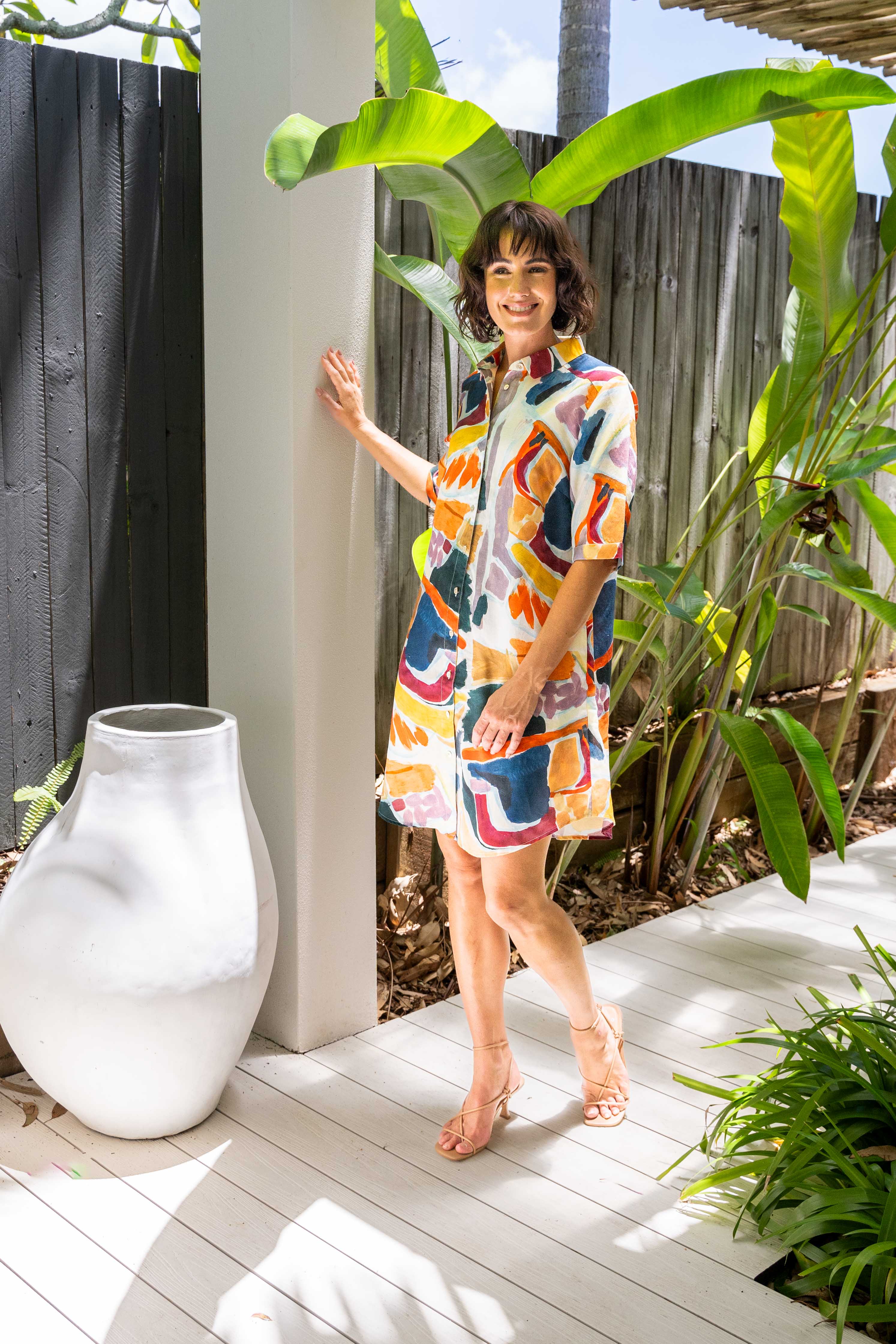 Woman in a colorful dress standing outdoors near a white vase and plants. See Saw Linen Shirtmaker Dress