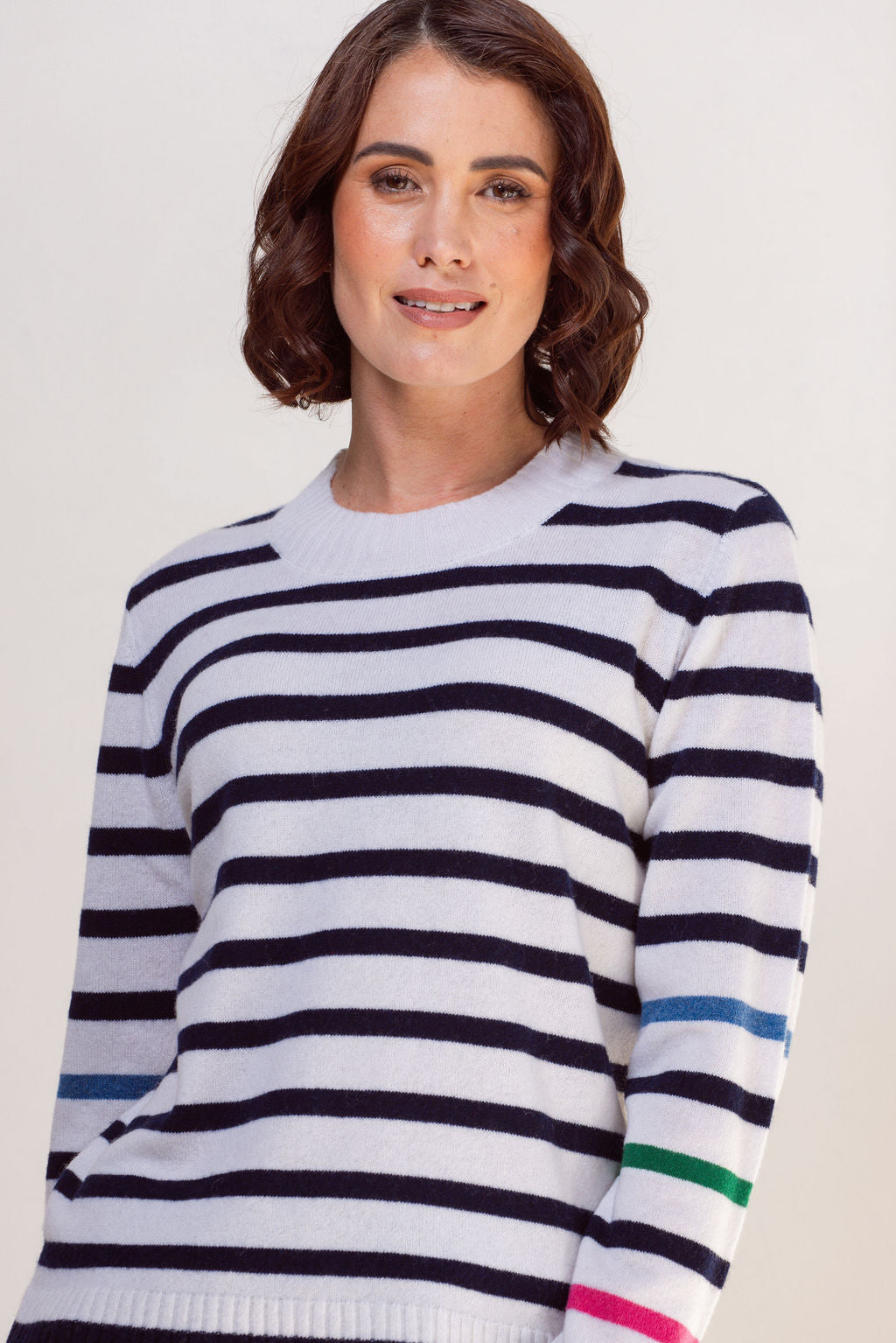 Woman wearing a striped See Saw sweater with colorful cuffs against a plain background