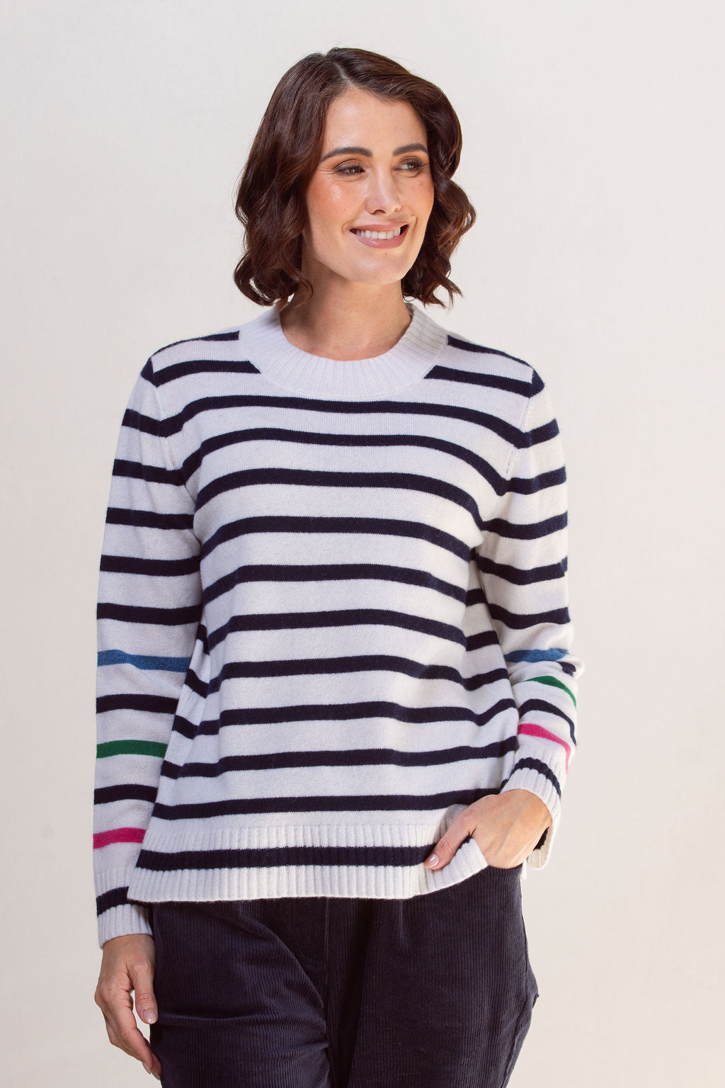 Woman wearing a striped See Saw sweater with colorful cuffs against a plain background