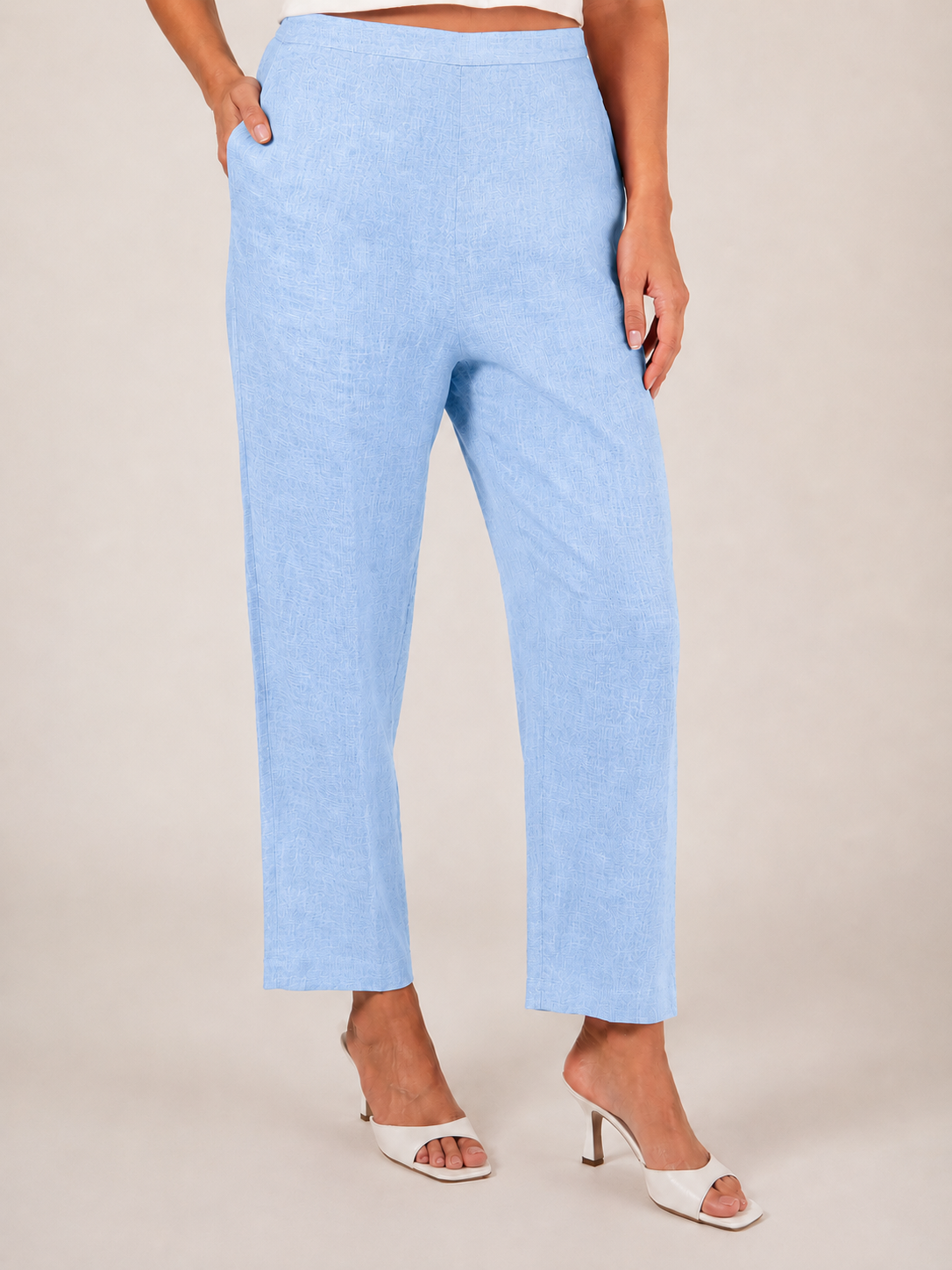 A person wearing sky blue See Saw 7/8 pants with a relaxed straight-leg fit, paired with white heeled slide sandals, photographed against a plain light beige studio background.