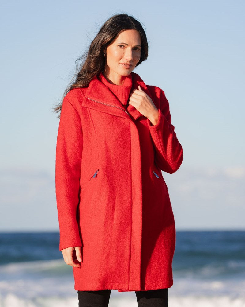 Woman wearing a boiled wool See Saw red coat on a beach with ocean and sky in the background