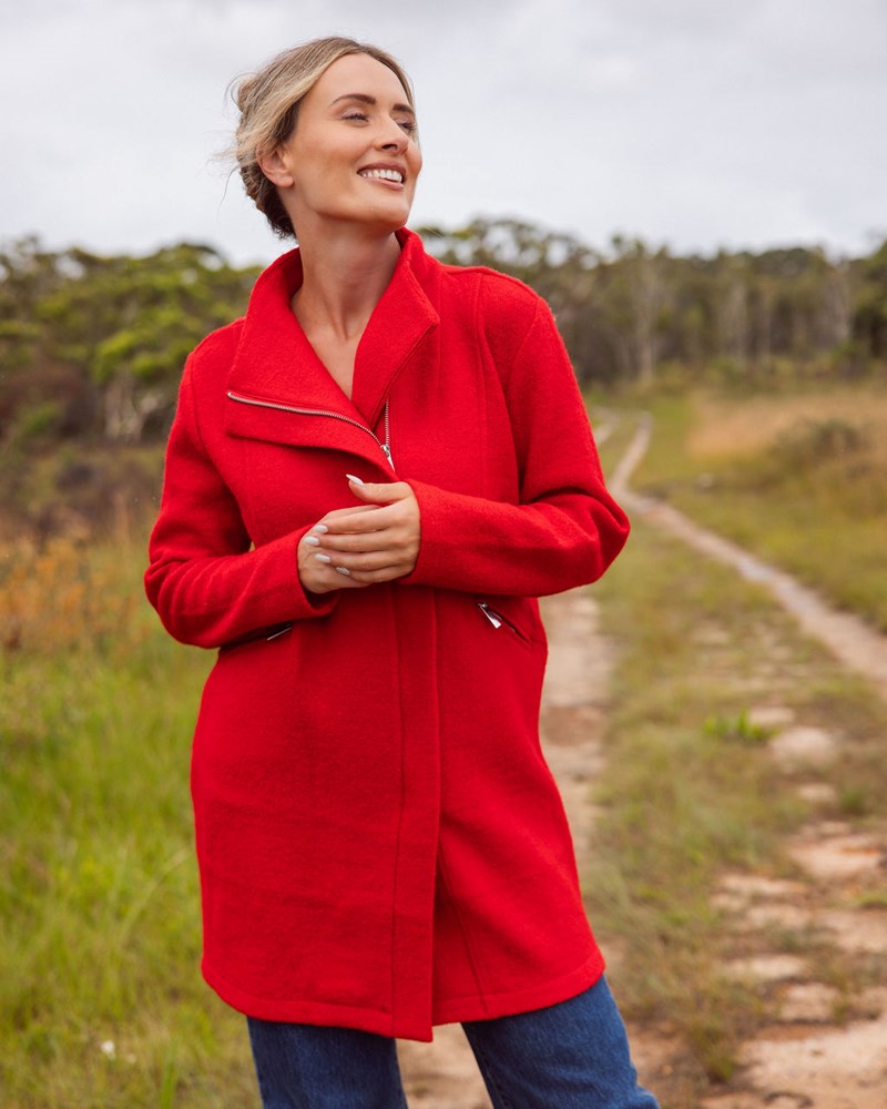 Woman wearing a See Saw boiled wool
red coat standing on a dirt path with trees in the background