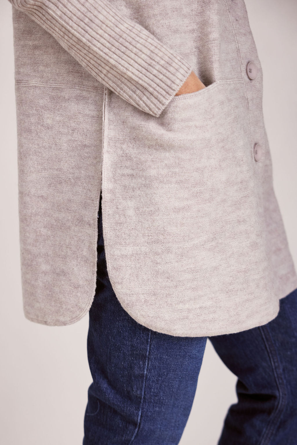 Woman wearing a long beige boiled wool See Saw cardigan on a plain background