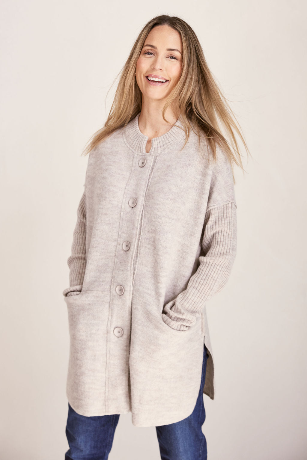 Woman wearing a long beige boiled wool See Saw cardigan on a plain background