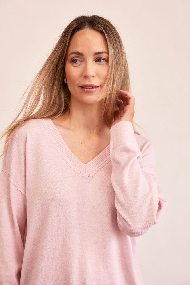 Woman wearing a light pink See Saw merino sweater and blue jeans on a beige background