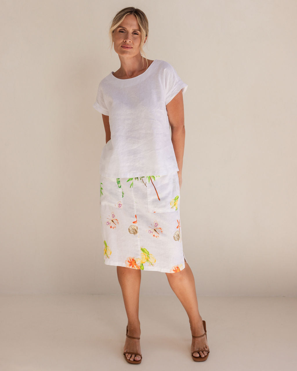 Woman in a white Linen See Saw top and pattern skirt standing in a minimalistic setting.
