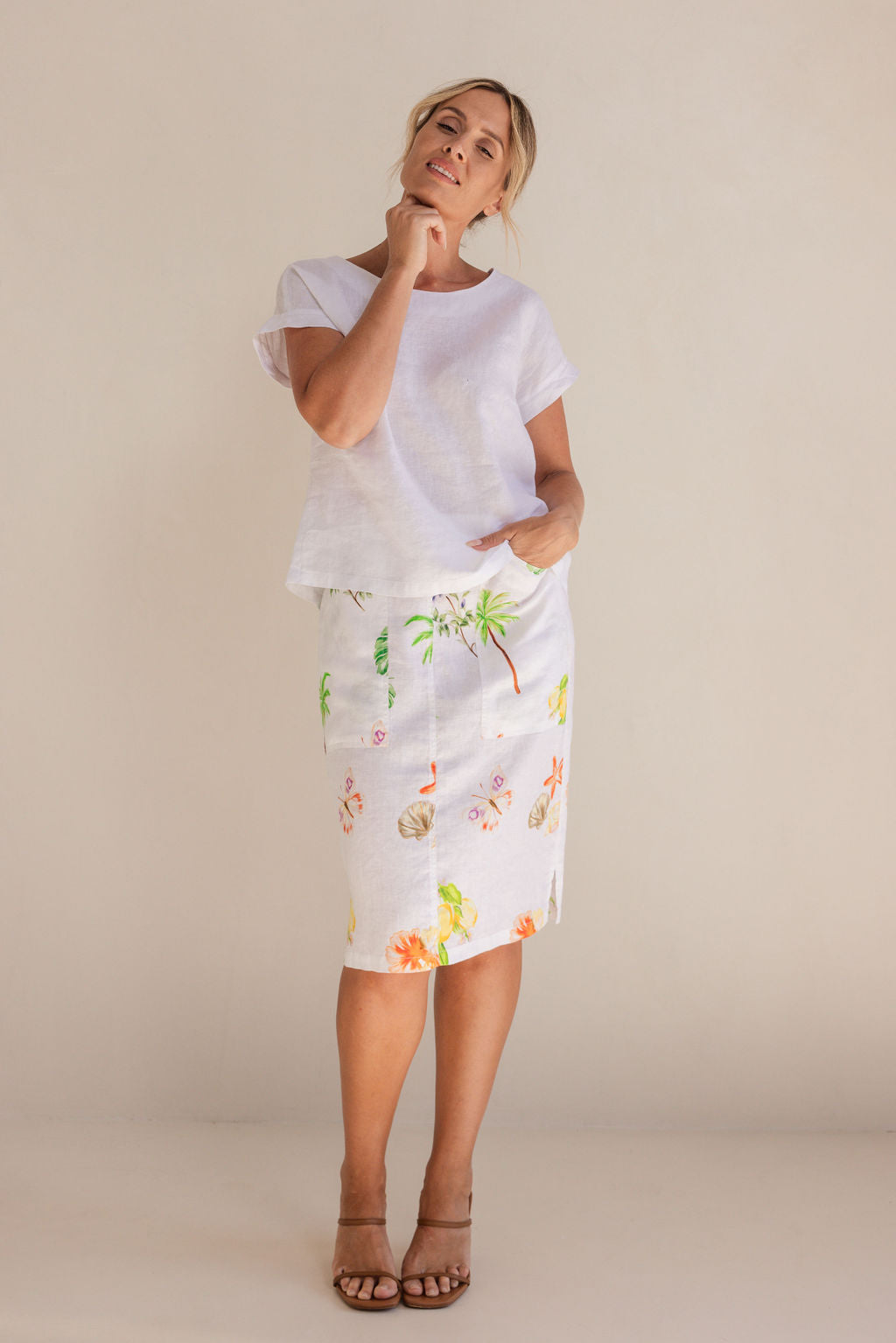 Woman in a white Linen See Saw top and pattern skirt standing in a minimalistic setting.