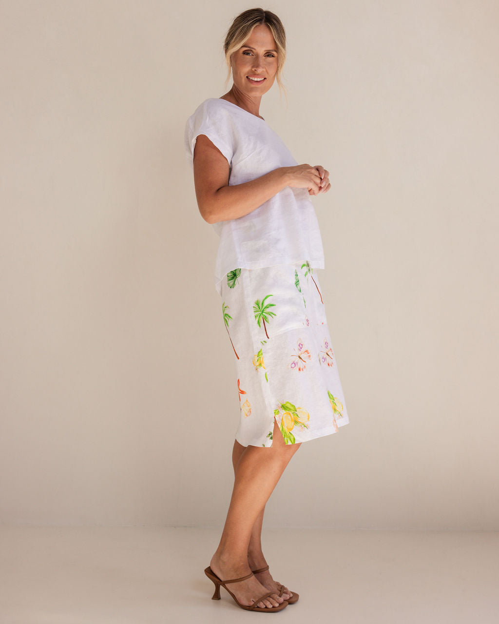 Woman in a white Linen See Saw top and pattern skirt standing in a minimalistic setting.