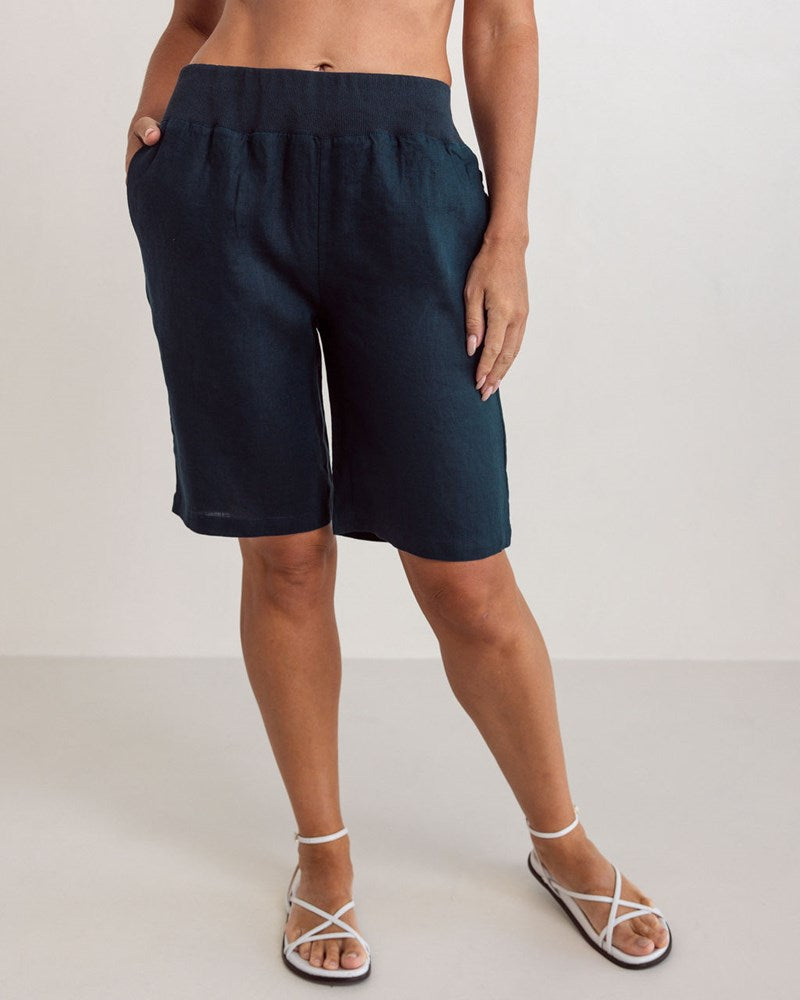 Woman wearing knee length navy linen See Saw shorts with an elastic waist against a white background.