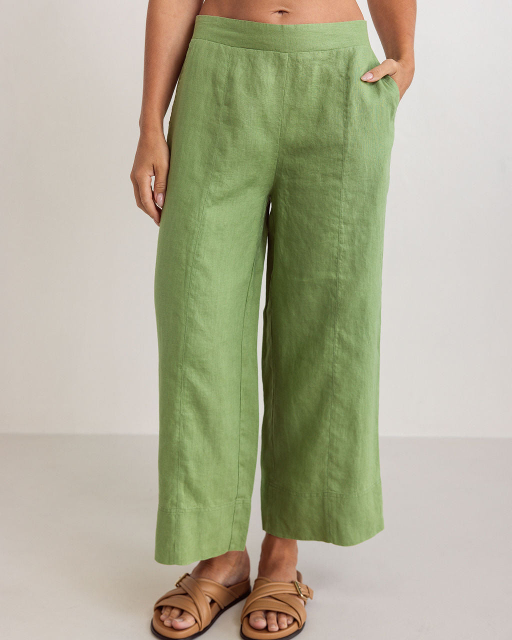 Woman wearing See Saw linen wide leg pants in pistachio with brown sandals against a white background