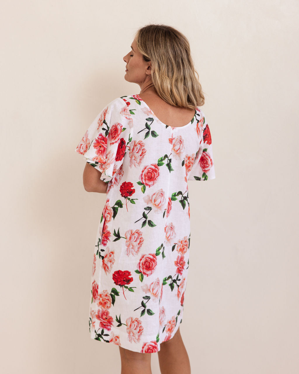 Woman wearing a See Saw linen flutter sleeve rose dress with a plain background