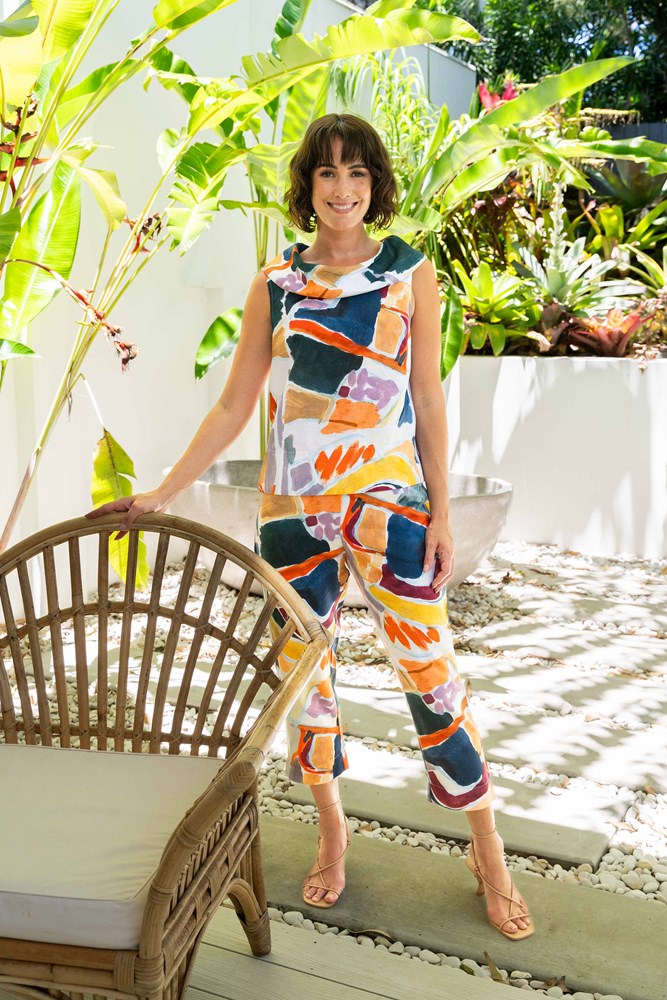 Woman in a colorful See Saw Linen pant set standing in a garden with plants and a chair.