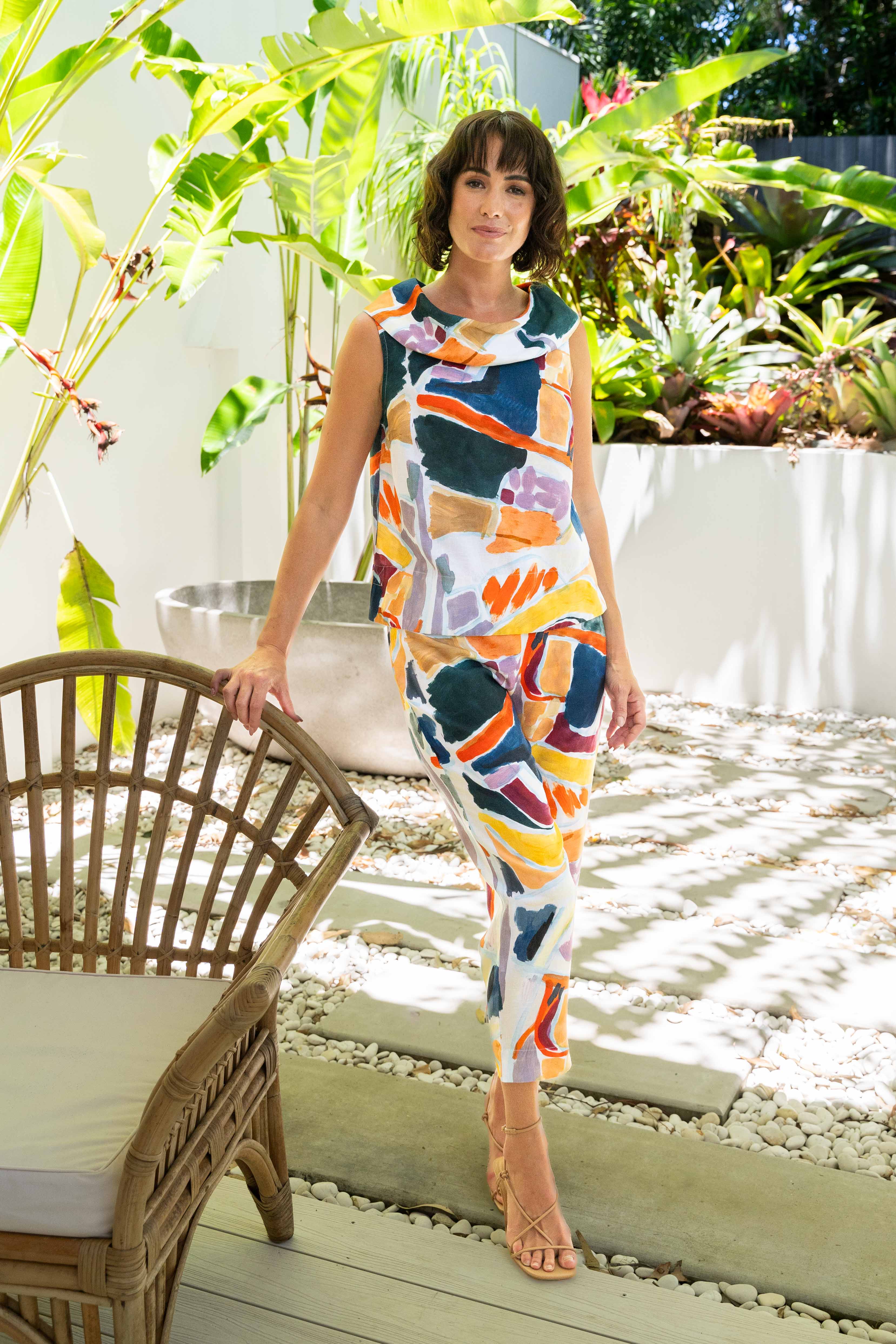 Woman in a colorful See Saw Linen pant set standing in a garden with plants and a chair.