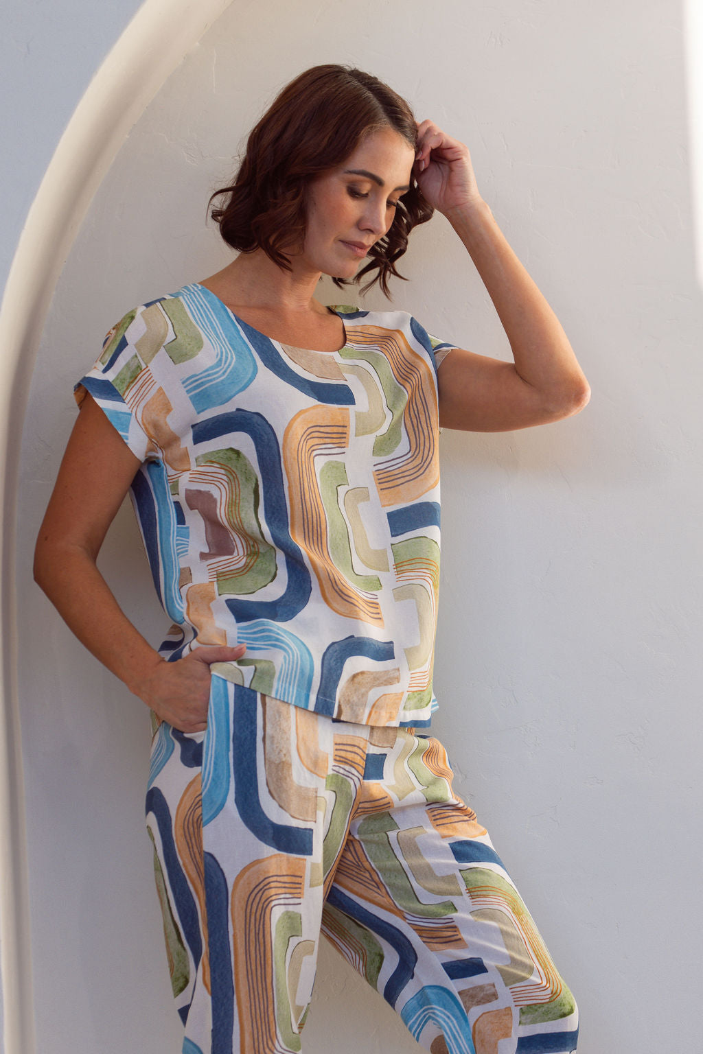 Woman wearing abstract See Saw seascape outfit standing in a bright, sunlit room with white walls and a plant.