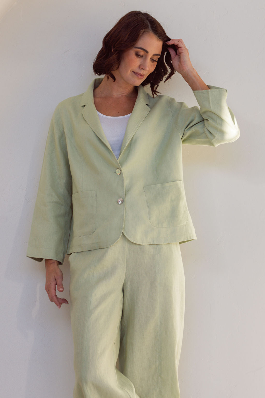 Woman in a light green Linen See Saw outfit standing in a minimalistic room with a plant.