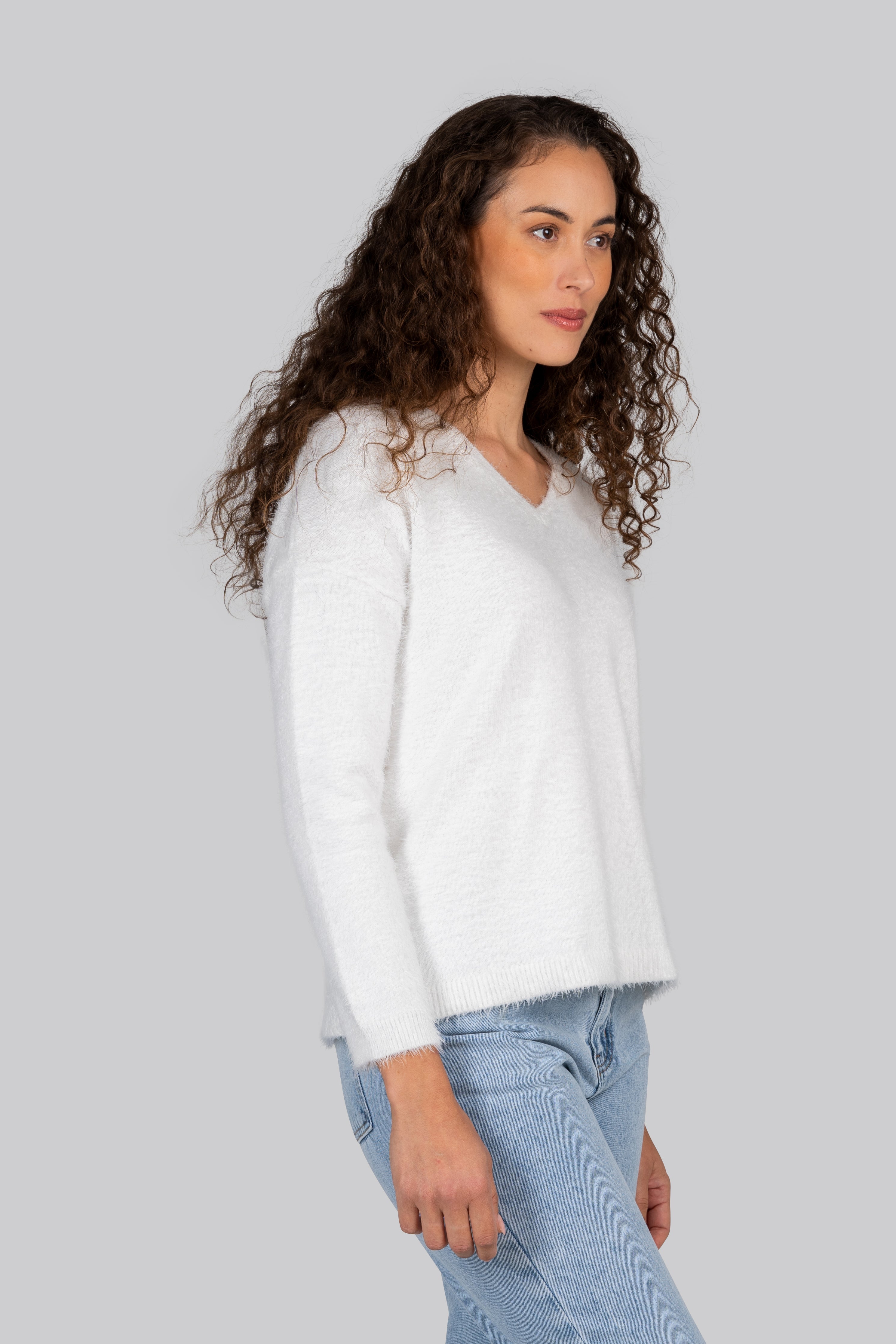 Woman wearing a white Kaleido textured sweater and colorful pants standing by a marina with boats in the background.