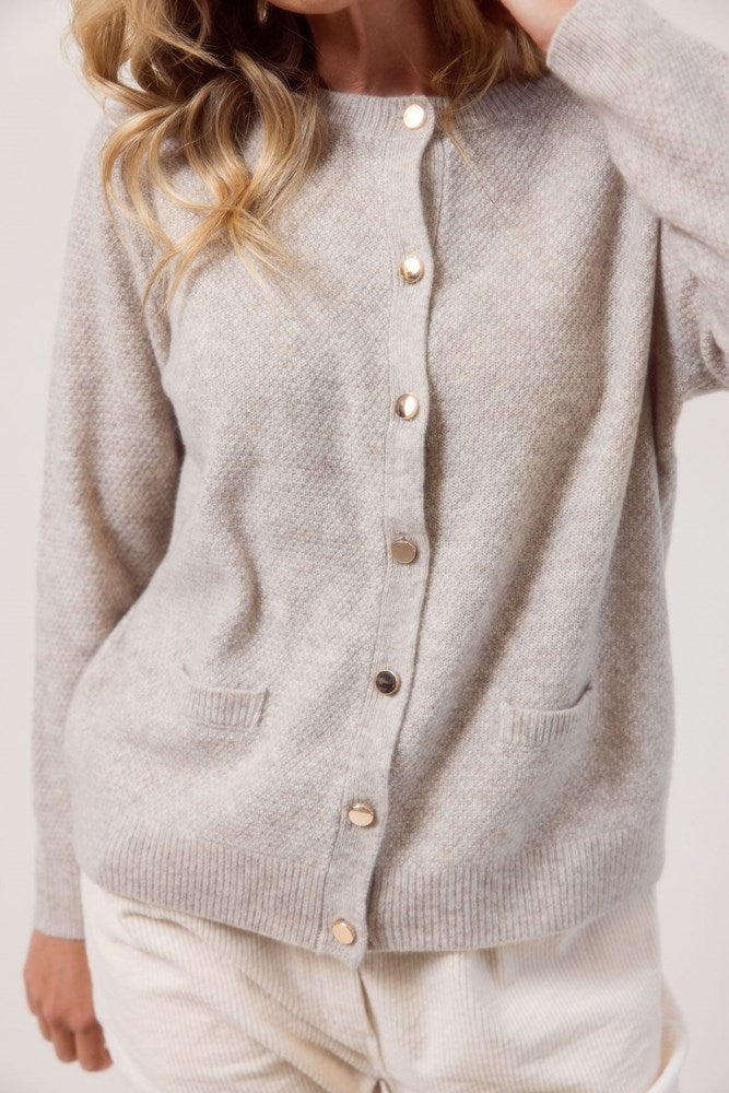 Woman wearing a wheat colour See Saw cardigan in wool and yak with buttons on a white background