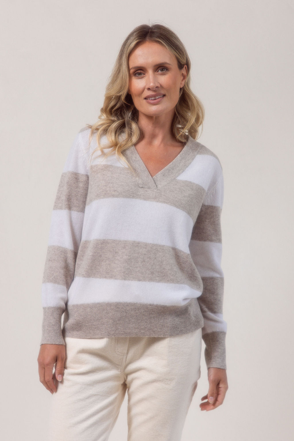 Woman wearing a striped Merino Wool See Saw sweater and beige pants against a plain background