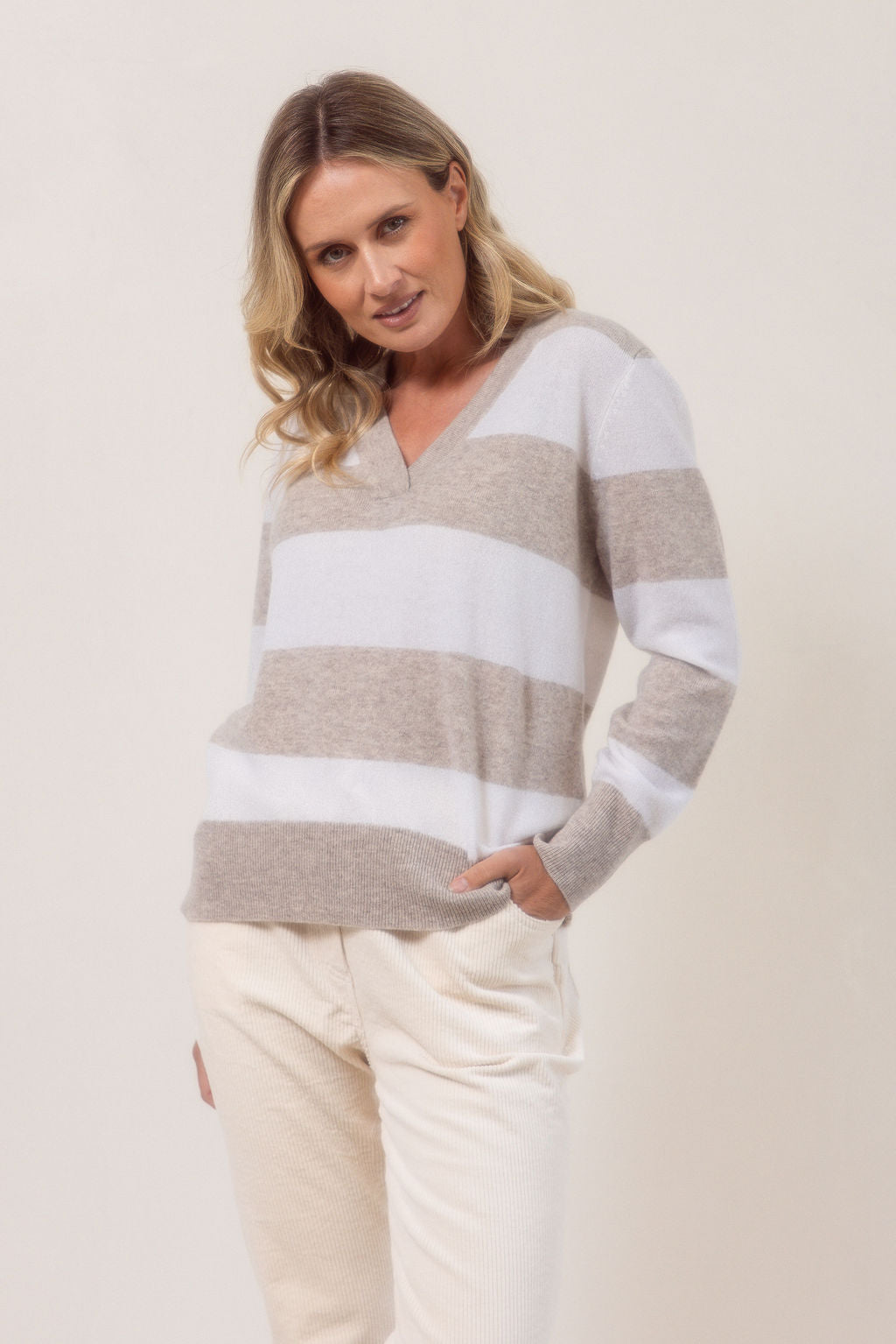 Woman wearing a striped Merino Wool See Saw sweater and beige pants against a plain background