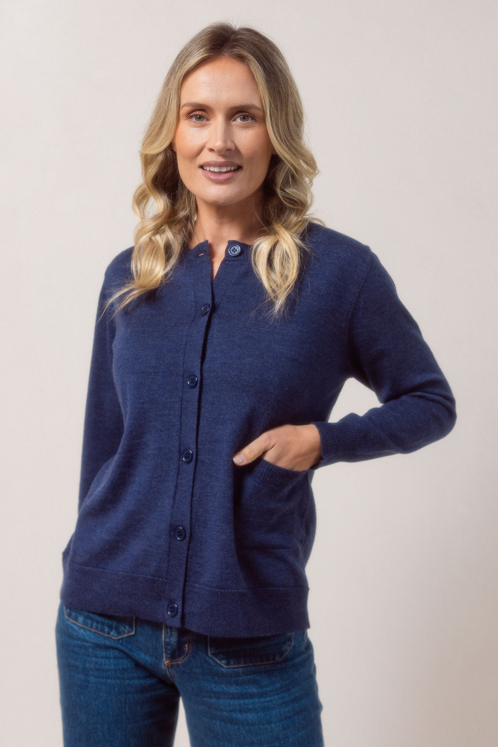 Woman wearing a merino wool See Saw indigo cardigan and blue jeans against a plain background