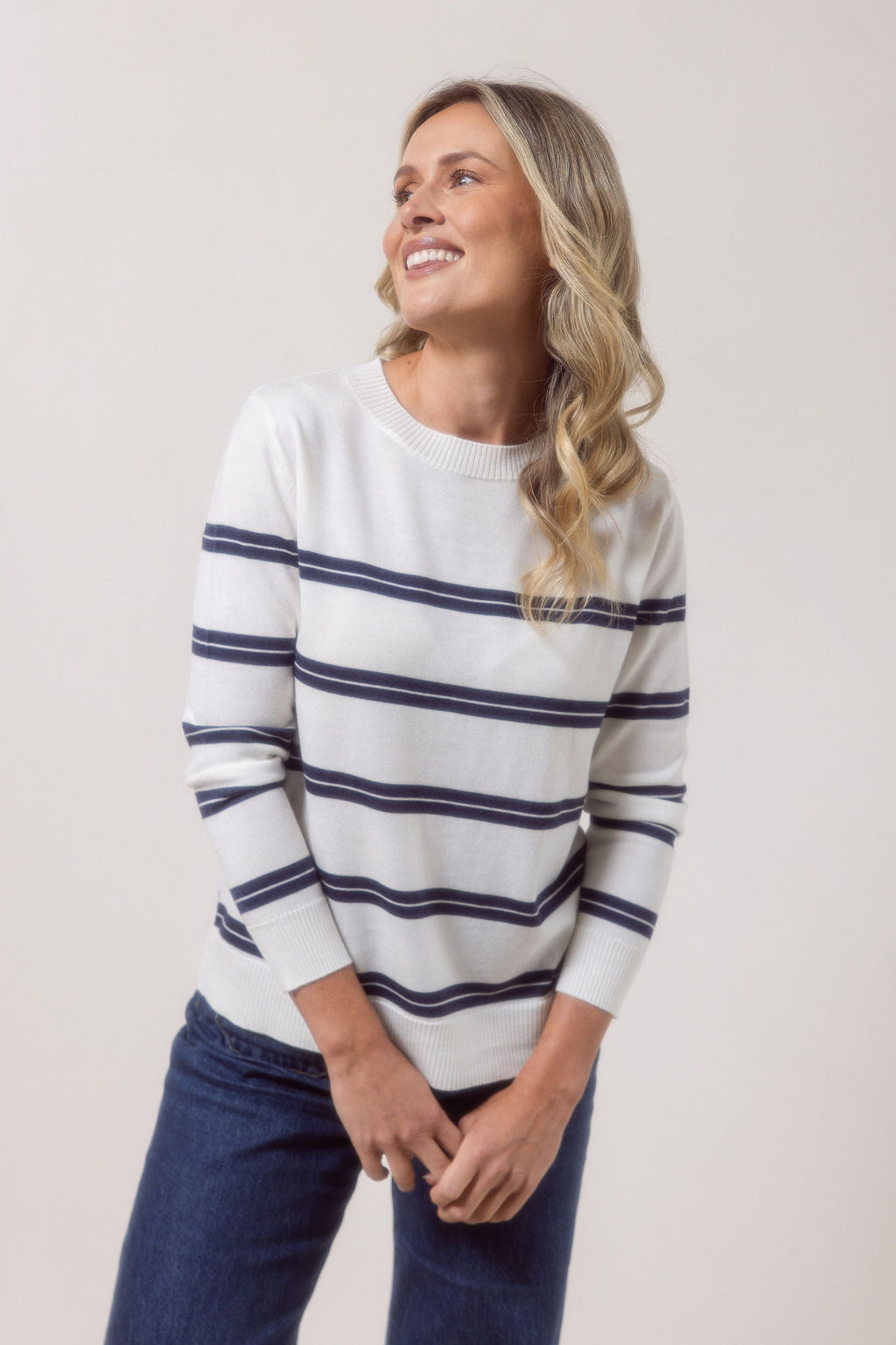 Woman wearing a white See Saw Merino wool sweater with blue stripes and dark jeans against a plain background