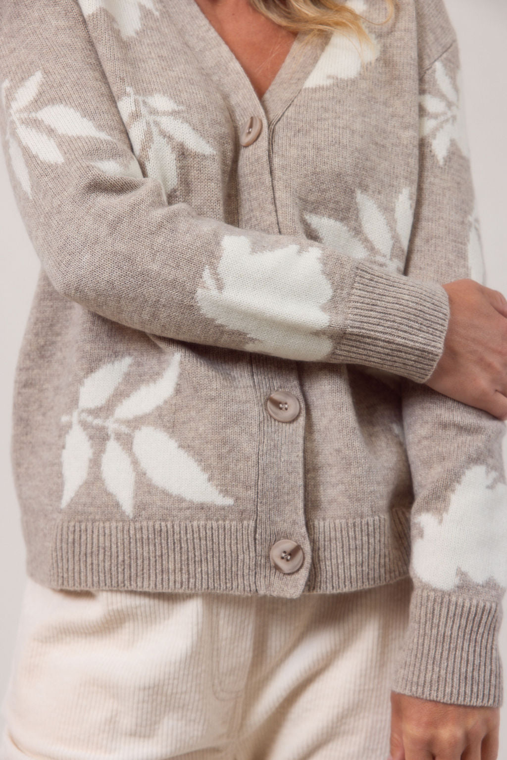 Woman wearing a oat See Saw cardigan with white floral patterns against a plain background