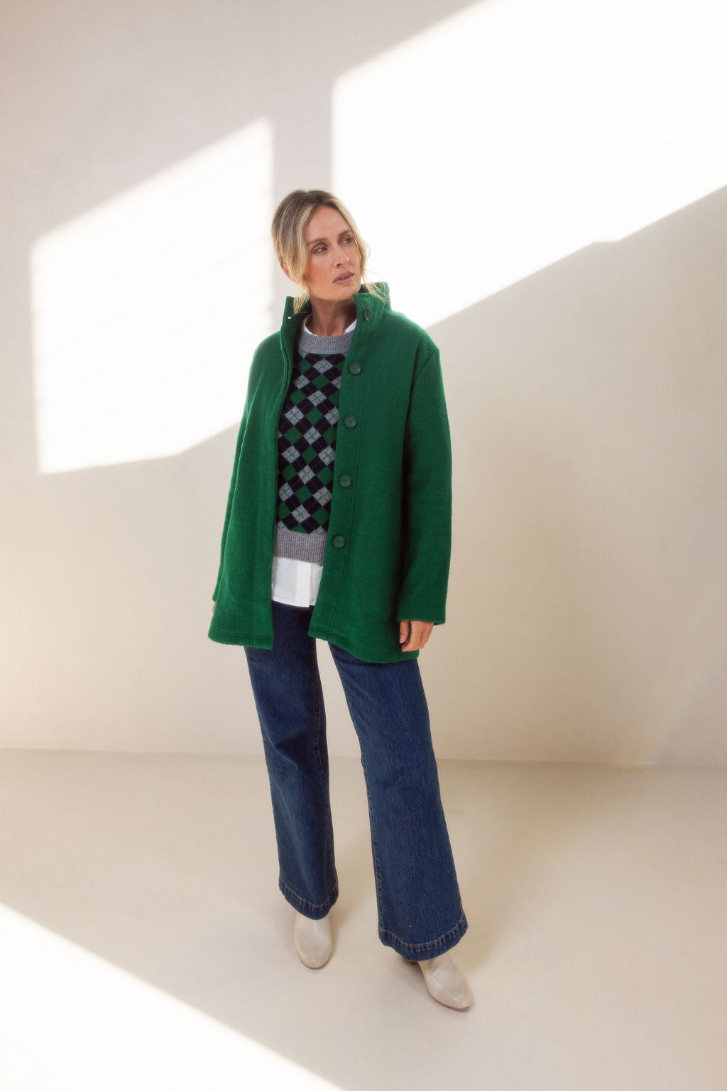 Woman wearing a green See Saw boiled wool jacket with funnel neck standing in front of a plain background